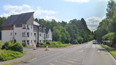 A wide road with white houses on the left