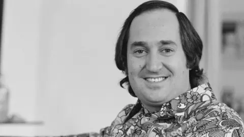 Neil Sedaka in a black and white photo wearing a 1970s style shirt