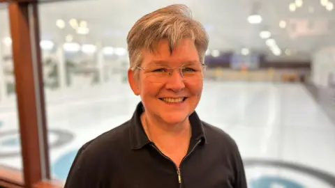 Gail Munro with short, grey hair wearing glasses and a black zip-up top smiling to camera