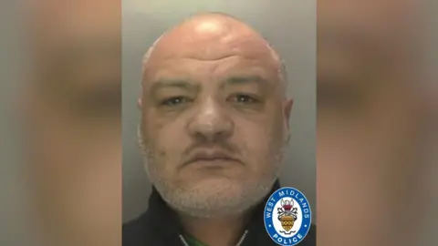 Mugshot of Conrad Byrd. He is bald and has a grey stubble beard and is looking at the camera 