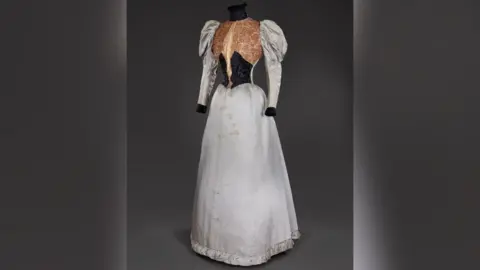 Historic Royal Palaces A slightly dirty, silver dress with puffy sleeves, the waist is black and the chest area is covered in gold detail. 