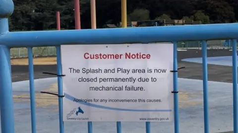 A sign on a blue fence stating the 'splash and play area is now permanently closed'