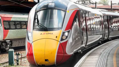 PA Media Modern looking red, white and yellow train at a station platform
