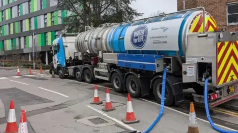 BBC A water truck pumping water into the network, with a line of cones in front of it