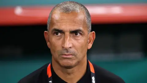 Close up of Sabri Lamouchi standing in the dugout looking focused