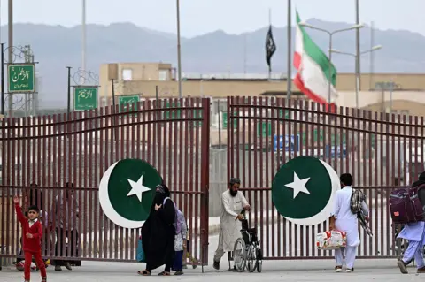 AFP via Getty Images Pakistanis walk across the Taftan border as they return from Iran, in Balochistan province, on March 9, 2026 amid ongoing US-Israel strikes on Iran. 