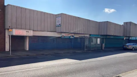 North East Lincolnshire Council Empty shop units along Osborne Street. They have flat concrete roofs and windows with blue metal shutters in front of them