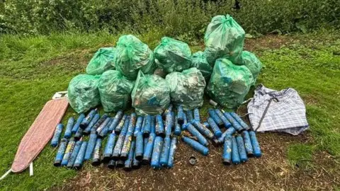 Peterborough Litter Wombles Association Blue canisters laid down on the grass next to green bin bags 