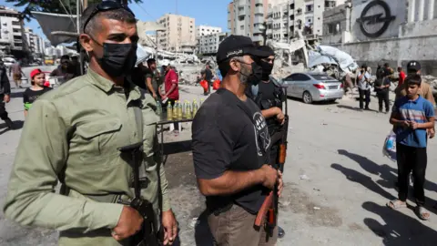 Reuters Three Hamas militants wearing face masks and carrying automatic weapons stand guard on a destroyed street in downtown Gaza. 