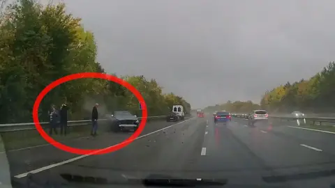 Kent Police Dashcam image of three people standing on the hardshoulder of a motorway. 
