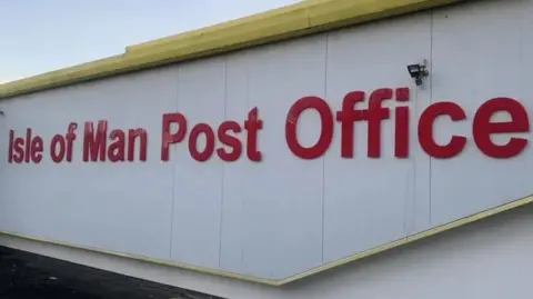 The outside of a one-storey, white flat-roofed industrial unit with Isle of Man Post Office on its wall in large red letters.