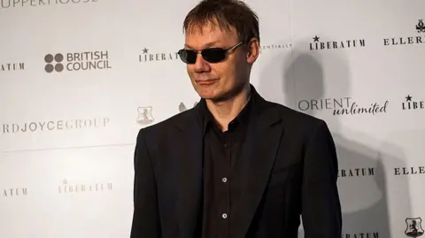 Getty Images Orbit wearing a black suit and sunglasses, slightly smiling on a red carpet