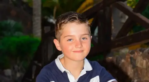 Supplied A young boy with brown hair wearing a blue and white polo smiling into the camera