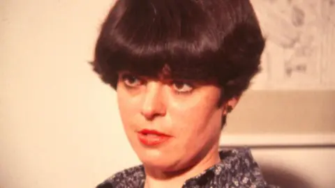 Felicity Grainger is interviewed in a room with a white wall and a painting behind her.