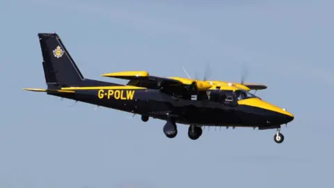 A stock image of a dark blue and yellow fixed wing police plane with the letters G-POLW printed on the side.