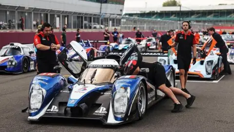 Silverstone Racing cars on the grid at Silverstone ahead of a race, with mechanics surrounding vehicles.