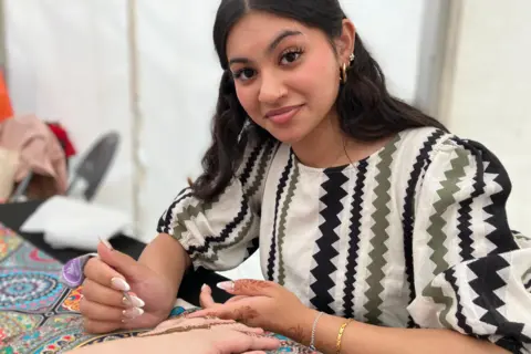 Jon Wright/BBC A woman is painting a henna tattoo on another woman's hand