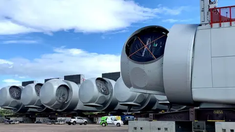 Wind turbine “nacelles” – very large wind farm generator components towering over parked vans before the turbines are built