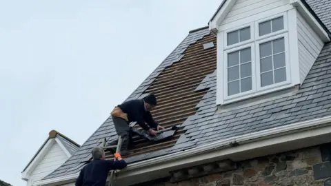 Two men on the roof of Lihou house putting a black under sheet down before replacing tiles.