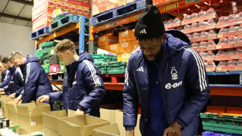 Nottingham Forest Nottingham Forest players help to package donated food into boxes as part of a drive to help struggling families across the city in 2023.