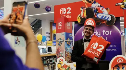 Bloomberg via Getty Images A customer takes a photograph with a Nintendo Switch 2 display board during the sale launch of the gaming console on Oxford Street in London early on 5 June 2025.