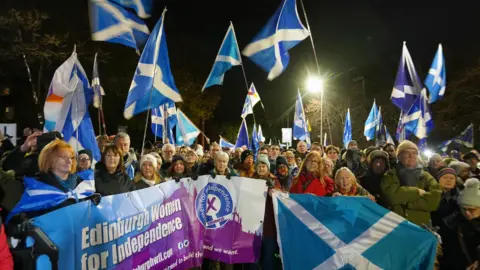PA Media Supporters of Scottish independence stand outside at night waving Saltires and signs supporting independence