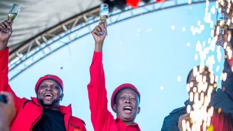 Getty Images Floyd Shivambu (kiri) dan Julius Malema (tengah) mengangkat gelas sampanye tinggi-tinggi di acara unjuk rasa ulang tahun ke-11 EFF di Kimberley, Afrika Selatan - 27 Juli 2024