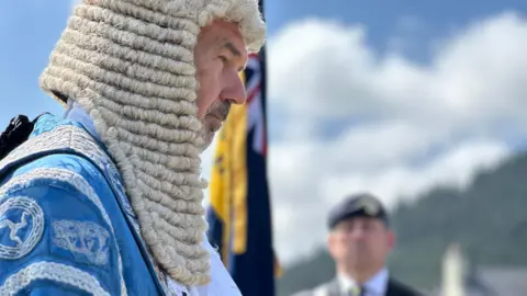 Skelly in the blue and silver robes and white wig of the president.