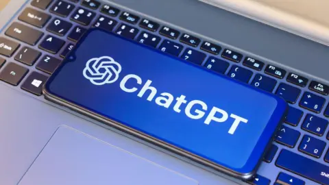 A laptop keyboard with a mobile phone on it. On the phone screen is a blue and white ChatGPT logo.
