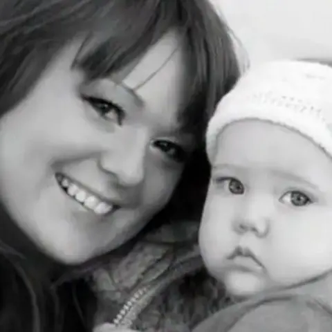 Family handout A woman with long hair is smiling while cuddling a baby wearing a light-coloured hat in this black and white photo.
