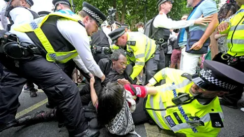 PA Media Police officers - one of whom is on the ground - hold down protesters
