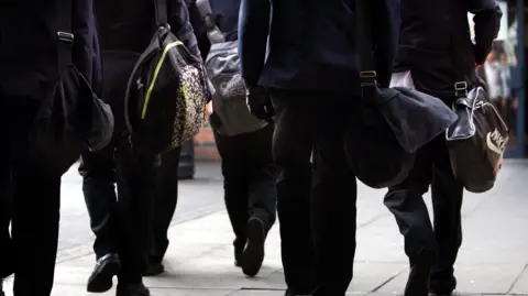 Picture shows children walking to school wearing a black uniform.