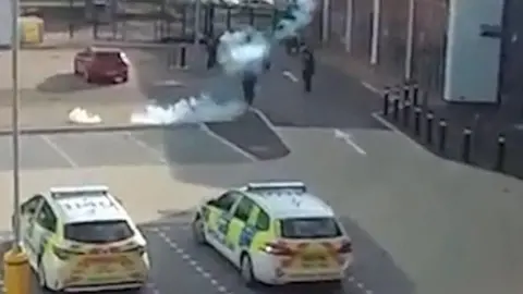 Derbyshire Police A screen grab of the police footage which shows a smoke from a stun grenade and two police cars in the foreground.