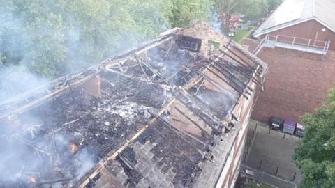 Aerial view of damaged roof of black of flats with smoke rising
