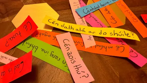 Colourful strips of paper are lying on a table. Each one has a different phrase written in Irish