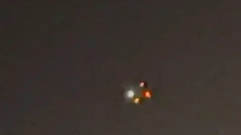 White, yellow and red lights shine in the sky from a drone in New York