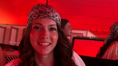 A head and shoulders image of a young woman smiling while wearing a bandana. 
