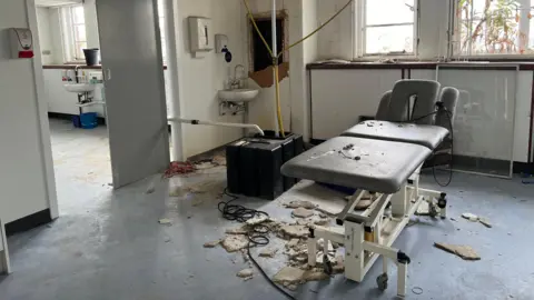 Crumbled plaster litters the floor of a hospital room.