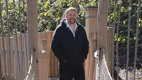 Supplied Jimmy Southern standing on a bridge with his hands in his pockets, smiling. 