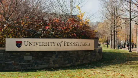 Getty Images Fall leaves and barren trees surround a brick sign reading "University of Pennsylvania" 