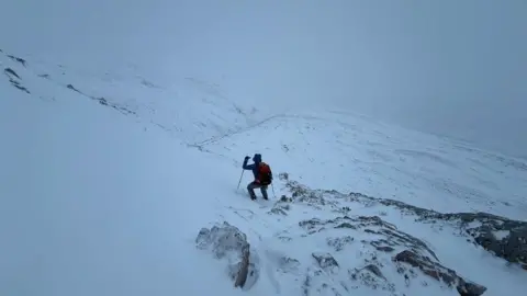 SAIS Torridon Man in walking gear with sticks on a mountain which is covered in snow