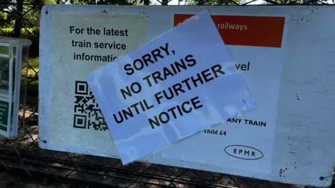 Jack Maclean/BBC A sign put up across a noticeboard that says: Sorry, no trains until further notice.