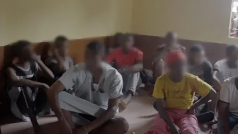 Young men and women sitting on a floor, their faces have been blurred. They were found in the house that was raided by police in Makeni.