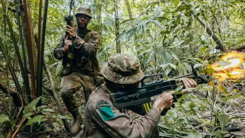 British Army Two soldiers holding guns and wearing camouflaged clothing. They are in the jungle. 