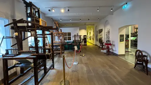 A large open white room with wooden contraptions littered throughout with red rope keeping people a safe distance away from them. 