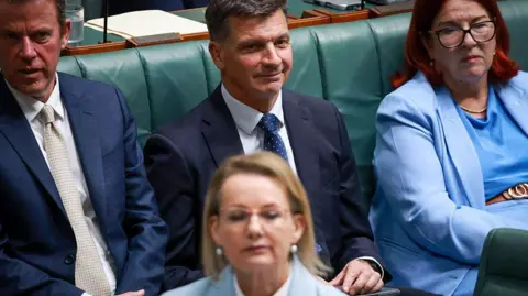 Getty Images Three politicians sitting on the frontbench in parliament with one female politician sitting at a desk in front.
