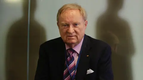 Ludwig Minelli, wearing a suit. 