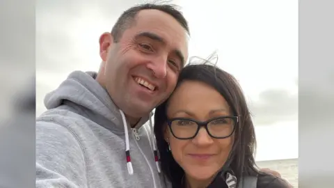A man and a woman taking a selfie together. The sea is in the background.
