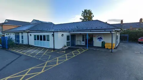 A single-storey building stands at the end of a large tarmacked area.