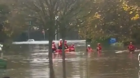 @JonesyMids9 A picture of people in red jackets and helmets in red boats on brown water with trees sticking up through it